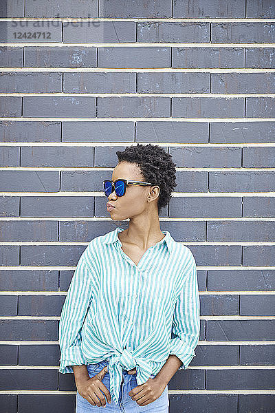 Woman with sunglasses standing in front of grey facade waiting
