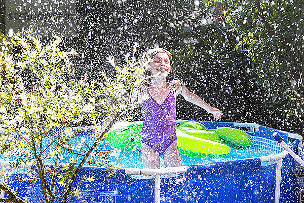 Laughing girl in paddling pool splashing with water