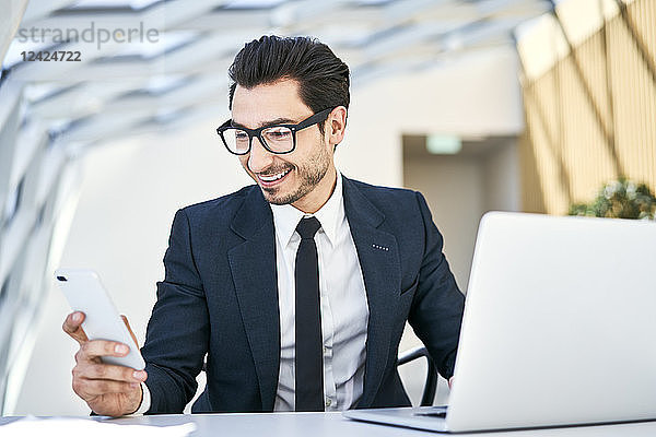 Smiling businessman looking at cell phone at desk in modern office