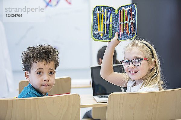 Portrait of schoolboy and schoolgirl with laptop and pencil case in class