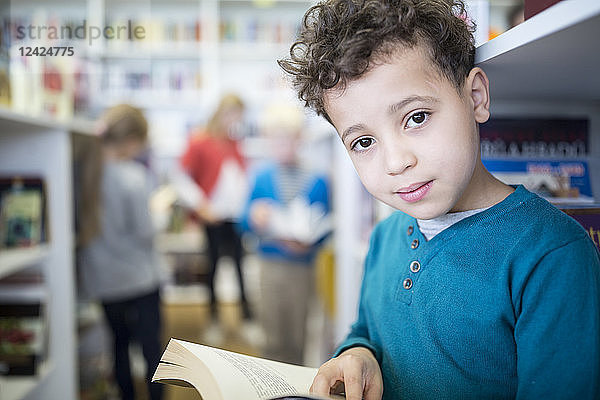 Portrait of smiling schoolboy with book in school library
