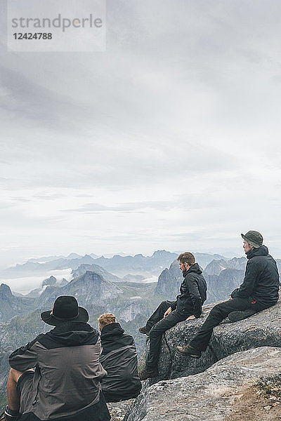 Norway  Lofoten  Moskenesoy  Young men sitting at Hermannsdalstinden  looking over Kjerkefjord