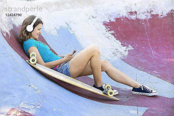 Female longboarder with earphones lying in halfpipe