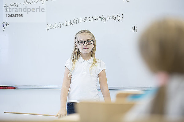 Schoolgirl standing at whiteboard with formula in class