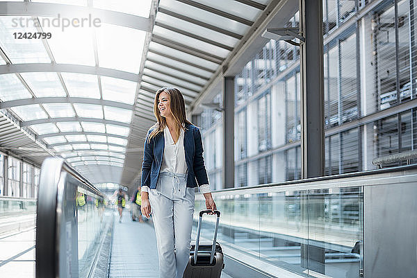 Smiling young businesswoman with baggage on moving walkway