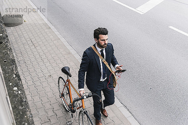 Businessman with bicycle and cell phone walking at the street