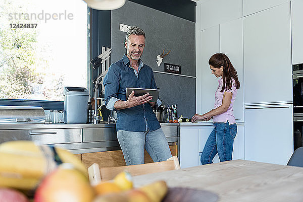 Couple in kitchen at home cooking and using a tablet