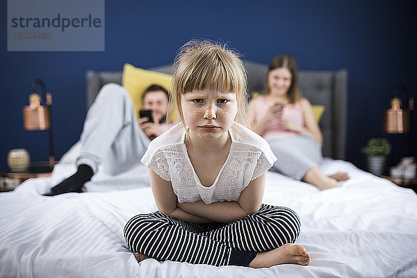 Angry little girl sitting on bed with her parents