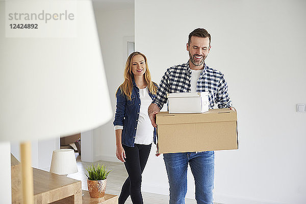 Happy couple moving into new flat carrying cardboard box