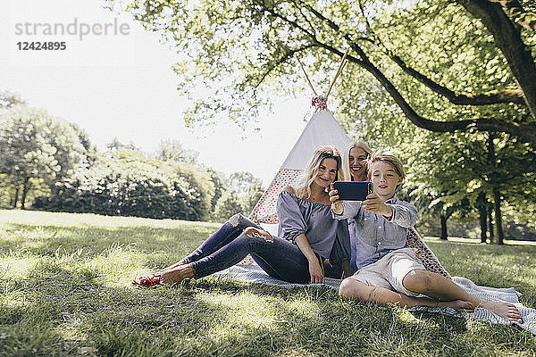 Two young women and a boy taking a selfie next to teepee in a park