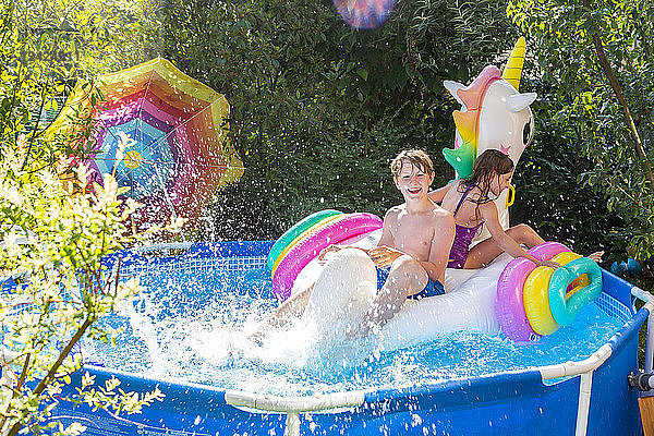 Brother and sister with oversized unicorn swim toy in paddling pool