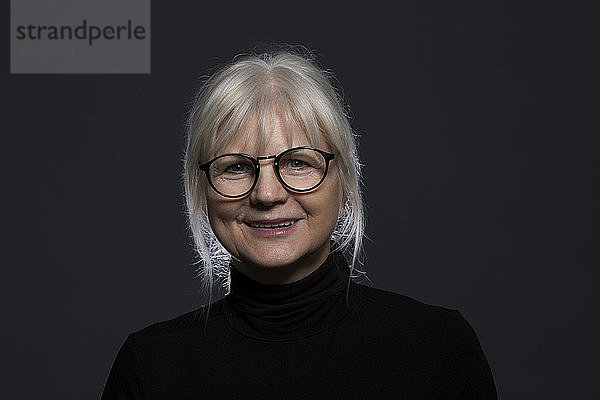 Portrait of smiling senior woman wearing glasses in front of dark background