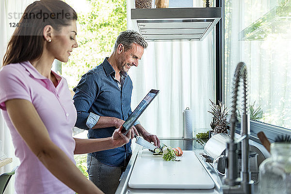 Couple in kitchen at home cooking and using a tablet