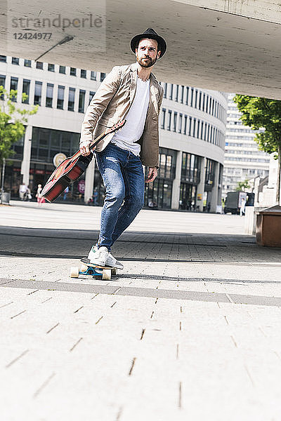 Young man with guitar riding skateboard in the city