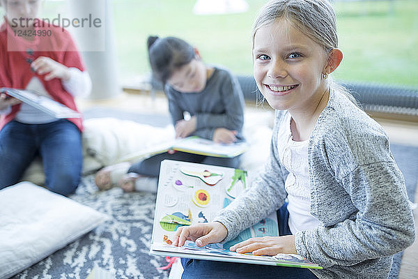 Portrait of smiling schoolgirl sitting on the floor with book in school break room