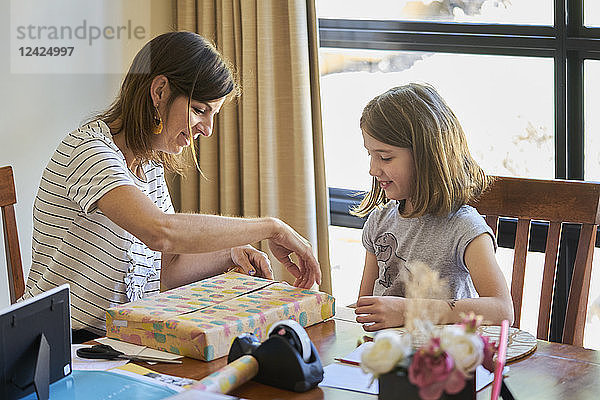 Mother and daughter packing gift at table at home