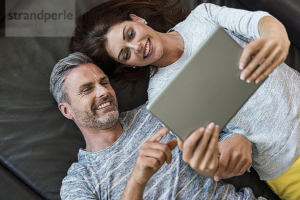 Happy couple lying on couch at home sharing a tablet