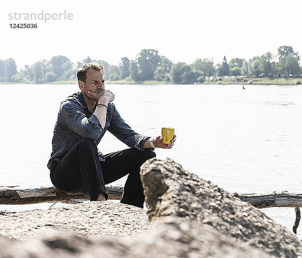 Mature man sitting at Rhine riverbank  looking at distance