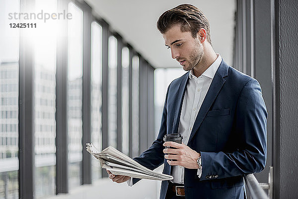 Young businessman standing in a passageway with takeaway coffee and newspaper