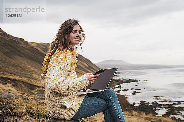 Iceland  woman using laptop and cell phone at the coast