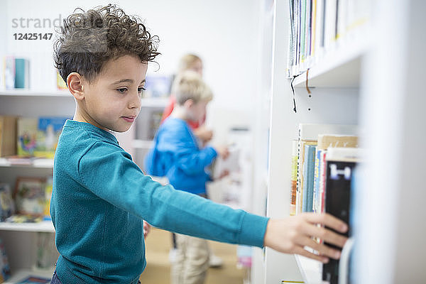 Schoolboy taking book from shelf in school library