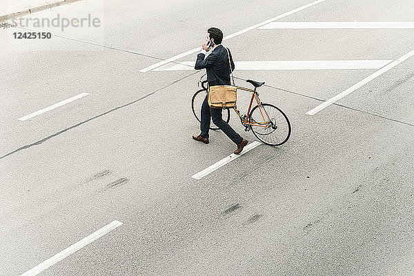 Businessman with bicycle on cell phone walking on the street