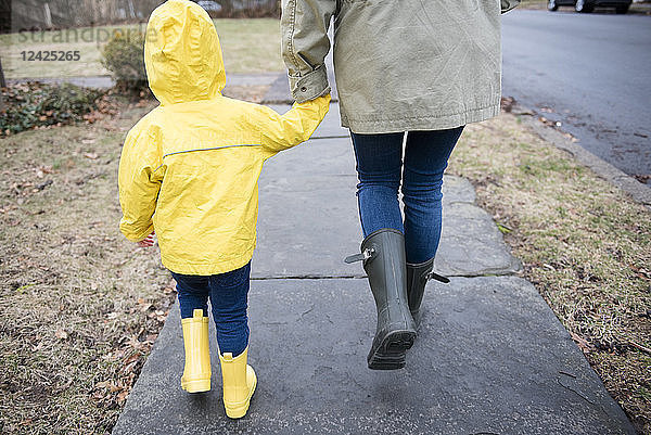 Mutter und Tochter (2-3) halten sich an den Händen und gehen an einem regnerischen Tag spazieren