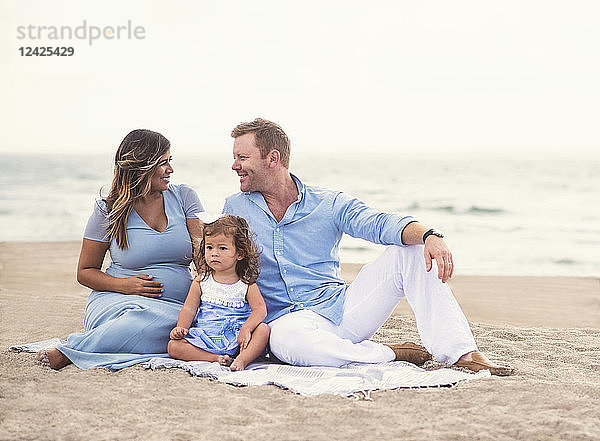 Familie sitzt auf einer Decke am Strand