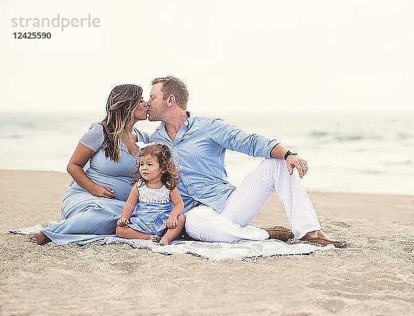 Familie sitzt auf einer Decke am Strand