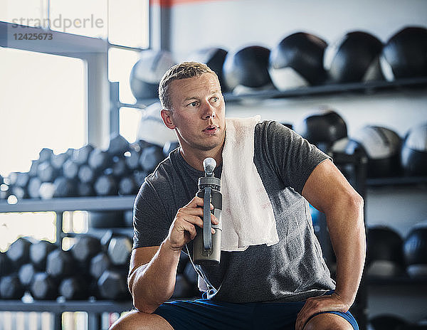 Mittlerer erwachsener Mann mit Handtuch und Flasche im Fitnessstudio