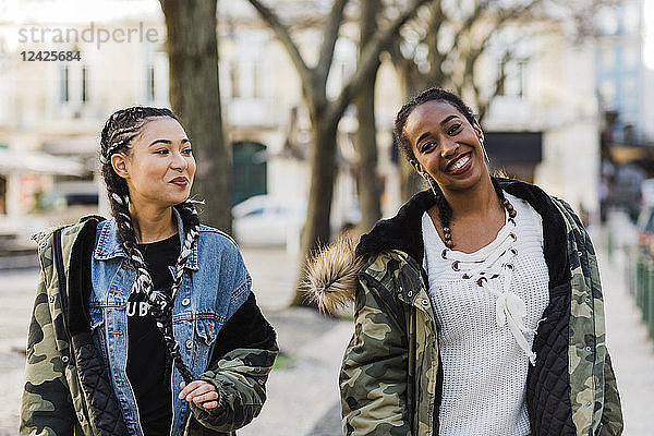 Zwei lächelnde junge Frauen gehen im Freien spazieren