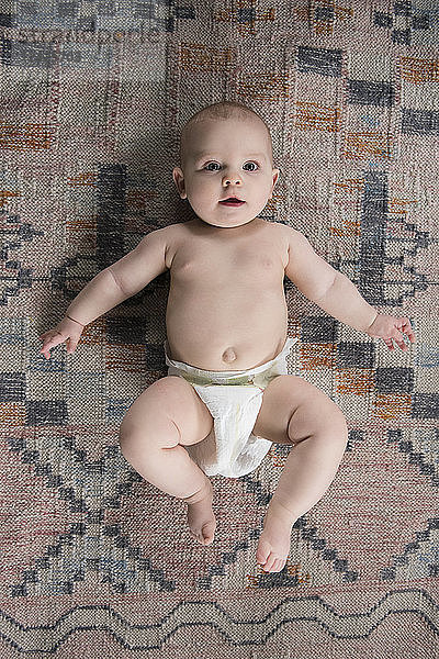 Baby (12-17 Monate) auf dem Teppich liegend