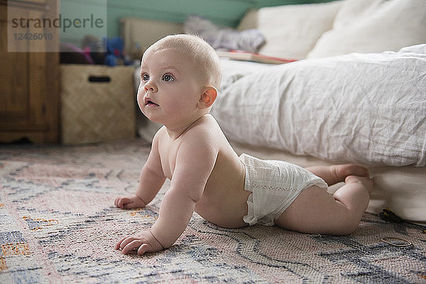 Kleines Mädchen (12-17 Monate) auf dem Teppich neben dem Sofa