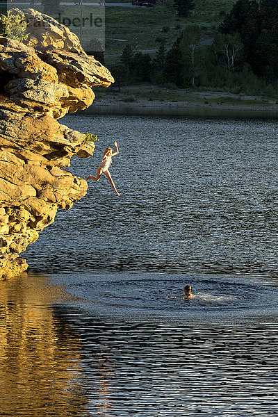 Abenteuerlustiges Mädchen springt von einem Felsen in einen See  Estes Park  Colorado  USA