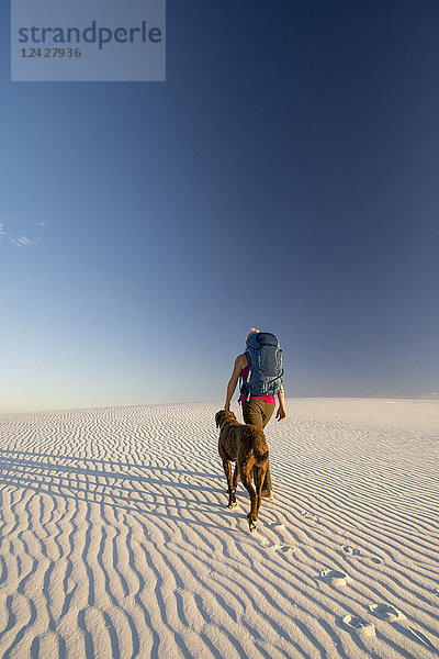 Rückansicht einer Rucksacktouristin mit Hund beim Wandern in der Wüste des White Sands National Monument  Alamogordo  New Mexico  USA