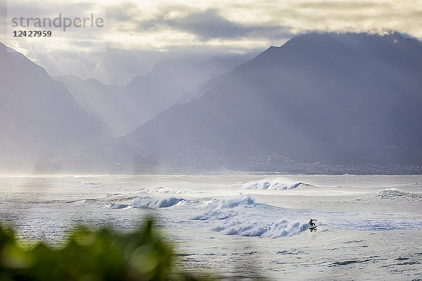 Entfernte Ansicht eines Surfers  der auf einer Welle im Meer reitet  Maui  Hawaii  USA