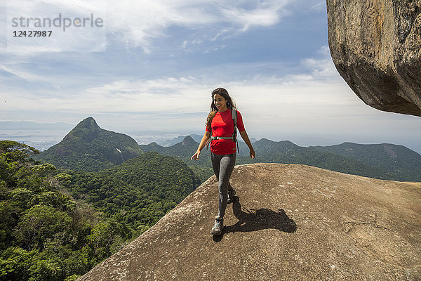 Vorderansicht einer einzelnen Wanderin  die auf einem felsigen Gipfel mit Blick auf die Berge wandert  Atlantischer Regenwald  Tijuca Forest National Park  Rio de Janeiro  Brasilien