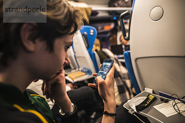 Jugendlicher sitzt im Zug und schaut auf sein Smartphone
