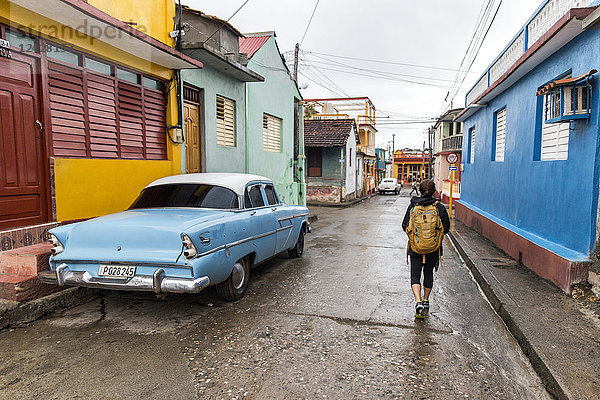 Rückansicht eines weiblichen Touristen  der mit einem Oldtimer in Baracoa  Provinz Guantanamo  Kuba  auf der Straße geht