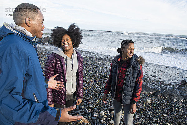 Drei lächelnde afroamerikanische Menschen stehen am Kiesstrand und unterhalten sich