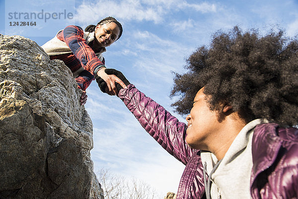 Eine junge afroamerikanische Frau hilft einer anderen Frau an einem sonnigen Tag auf einen Felsen