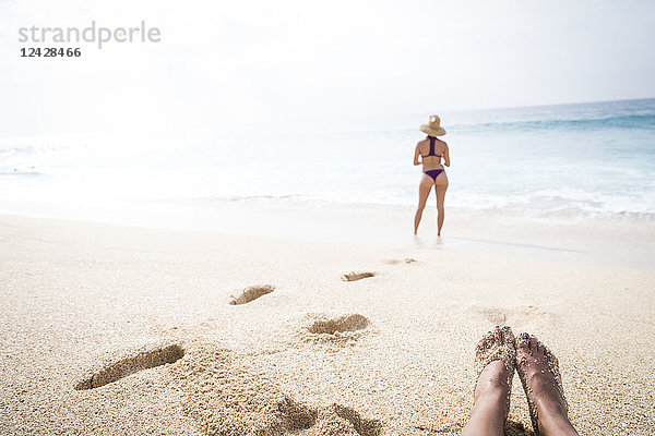 Rückansicht einer am Strand stehenden Frau und Füße eines anderen