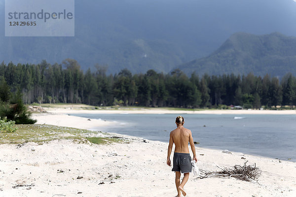 Rückansicht eines einzelnen Mannes ohne Hemd  der am Strand spazieren geht  Banda Aceh  Sumatra  Indonesien