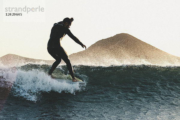 Seitenansicht von Longboard-Surfer in Neoprenanzug Reiten Welle im Meer bei Sonnenuntergang Schuss