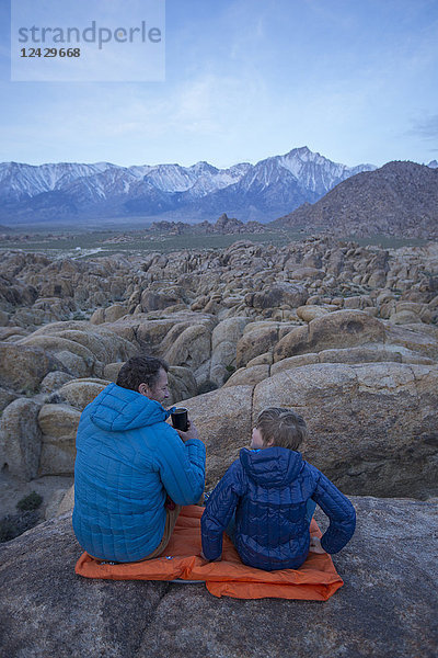 Vater und Sohn sitzen in der Alabama Hills Recreation Area mit den Sierra Nevada Mountains im Hintergrund  Lone Pine  Kalifornien  USA