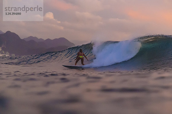 Rückansicht einer Surferin im Bikini auf einer Welle bei Sonnenuntergang