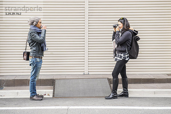 Seitenansicht einer asiatischen Frau  die einen Mann mit einer Kamera auf der Straße fotografiert