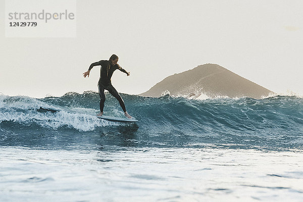 Surfer im Neoprenanzug auf einer Welle im Meer bei Sonnenuntergang in voller Länge