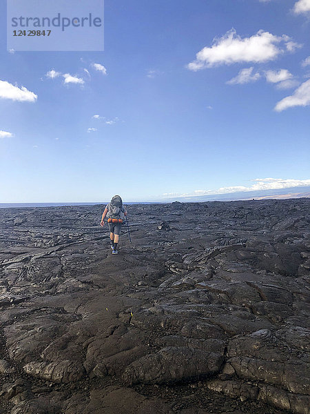 Ein Mann mit Rucksack wandert über alte Lavaströme  von Steinhaufen zu Steinhaufen auf einem kaum sichtbaren Pfad entlang des berühmten Puna Coast Trail zum Halape Beach. Der Weg ist ein 11 3 Meilen langer  schroffer Wanderweg für Rucksacktouristen ohne Schatten und Wasser im extremen Terrain des Hawaii Volcanoes National Park auf Big Island  Hawaii Islands  USA