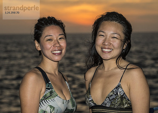 Porträt von zwei lächelnden asiatischen Frauen am Meer bei Sonnenuntergang